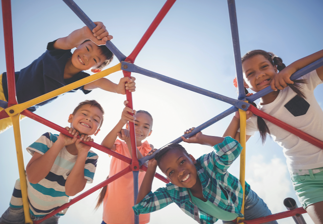 Photo of elementary kids playing on playground equipment, diverse group, blue sky sunny day