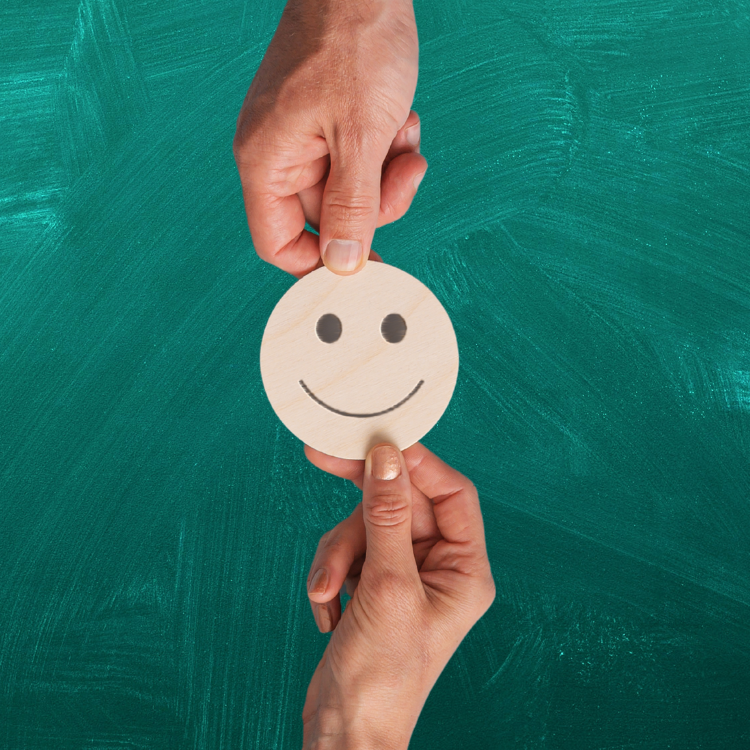 Smiley face exchanged between two hands, with green chalkboard behind it. 