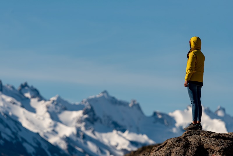 woman standing atop a mountain, looking out at mountain peaks. 