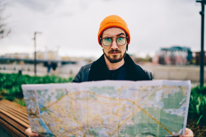 Confused man holding a map, one eyebrow raised. 