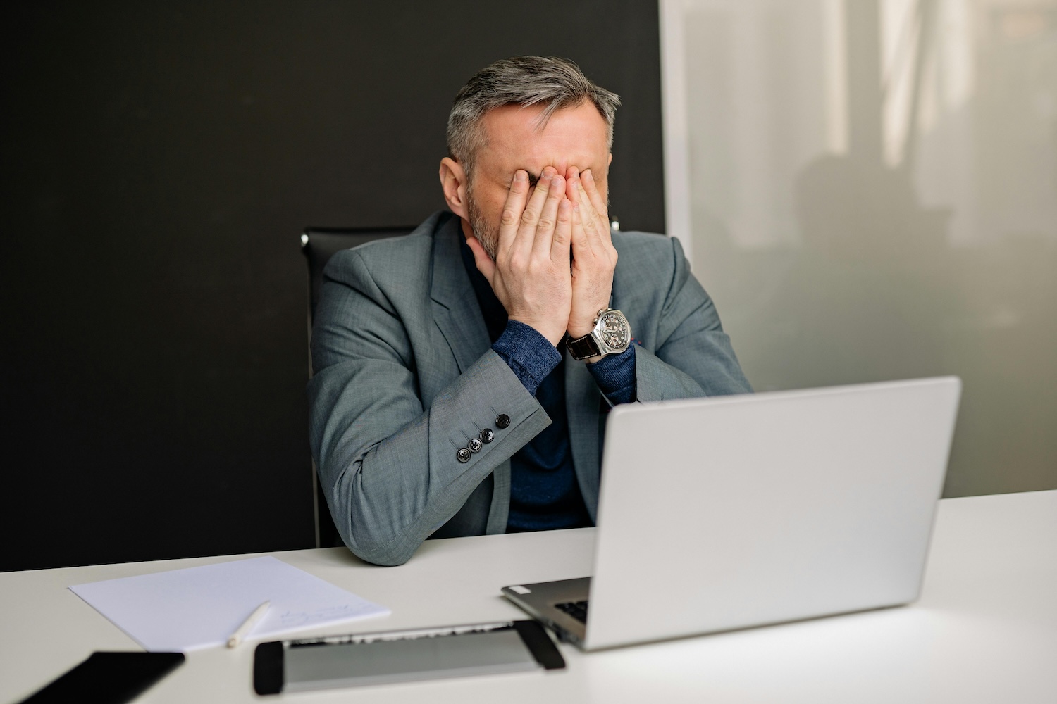 Frustrated man sitting behind a laptop with his face in his hands